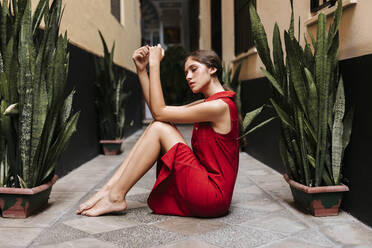 Porträt eines weiblichen Teenagers in einem roten Trägerkleid vor einer Wand - TCEF00185