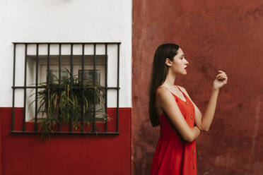 Portrait of female teenager wearing red strap dress in front of a wall - TCEF00187