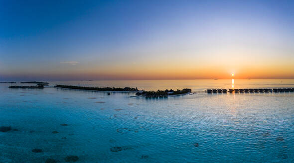 Malediven, Blick aus dem Hubschrauber auf die Bungalows der Ferienanlage, die sich entlang der Küste der Insel Maadhoo bei Sonnenuntergang erstrecken - AMF07887