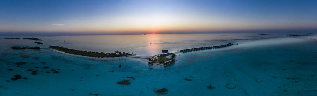Malediven, Blick aus dem Hubschrauber auf die Bungalows der Ferienanlage, die sich entlang der Küste der Insel Maadhoo bei Sonnenuntergang erstrecken - AMF07890