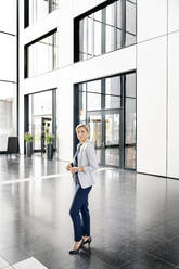 Successful businesswoman standing in entrance hall of office building - PESF01862