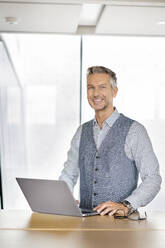 Porträt eines lächelnden Geschäftsmannes, mit Laptp - PESF01903