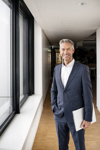 Businessman with laptop in corridor of office building stock photo