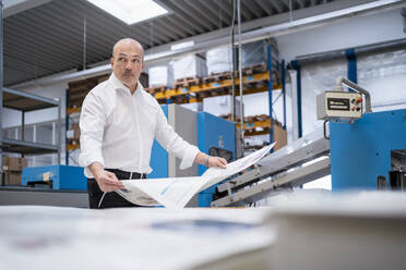 Geschäftsmann in einer Druckerei mit Papier in der Hand - DIGF09328