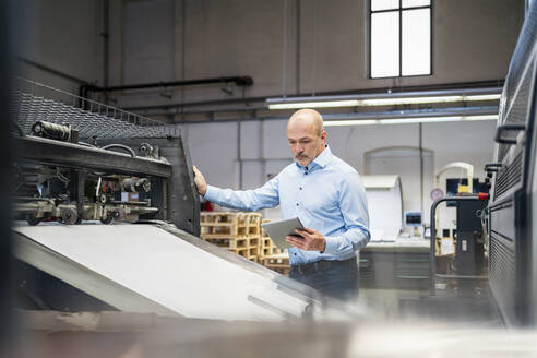 Businessman with tablet examining machine in a factory - DIGF09366