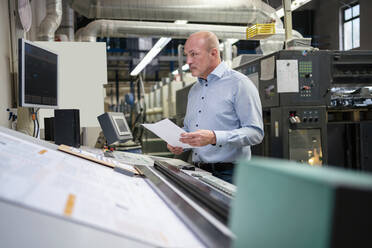 Businessman holding paper at a machine in a factory - DIGF09377