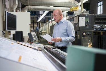 Geschäftsmann hält Papier an einer Maschine in einer Fabrik - DIGF09377