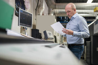 Geschäftsmann hält Papier an einer Maschine in einer Fabrik - DIGF09378