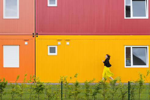 Frau läuft vor einem bunten zweistöckigen Containergebäude - HBIF00059