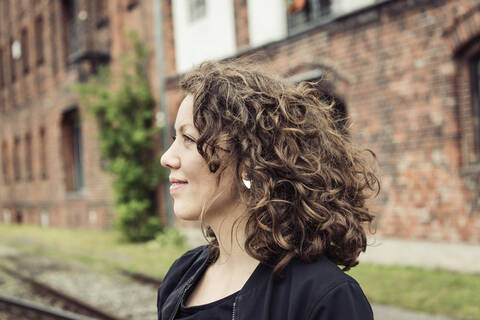 Smiling brunette woman with curly hair in front of a brick building and old rail tracks stock photo