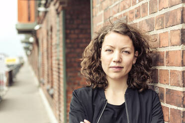 Portrait of smiling brunette woman leaning against a brick building - HBIF00068