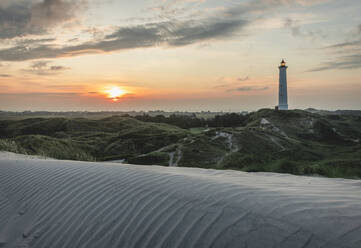 Denmark, Hvide Sande, Rippled sand dune at sunset with lighthouse in background - KEBF01464