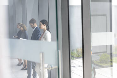Geschäftsleute, die in einem Bürogebäude warten und sich an eine Glasscheibe lehnen - BMOF00250