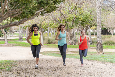 Drei sportliche junge Frauen laufen in einem Park - DLTSF00576