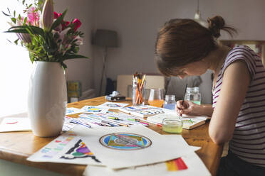 Frau sitzt am Schreibtisch und malt mit Aquarellfarben - WPEF02681