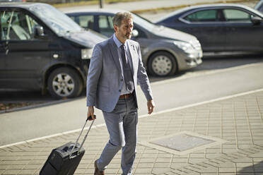 Geschäftsmann mit Gepäck auf Rädern auf dem Bürgersteig - ZEDF02950