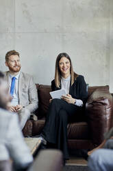 Glücklicher Geschäftsmann und Geschäftsfrau sitzen auf einer Couch in der Hotellobby während einer Besprechung - ZEDF02980