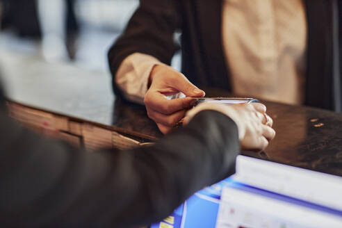 Close-up of woman paying contactless with credit card at reception desk - ZEDF03000