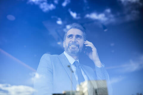 Porträt eines reifen Geschäftsmannes am Telefon hinter einer Fensterscheibe, lizenzfreies Stockfoto