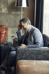 Lächelnder Geschäftsmann mit Laptop und Smartphone in der Hotellobby - ZEDF03016