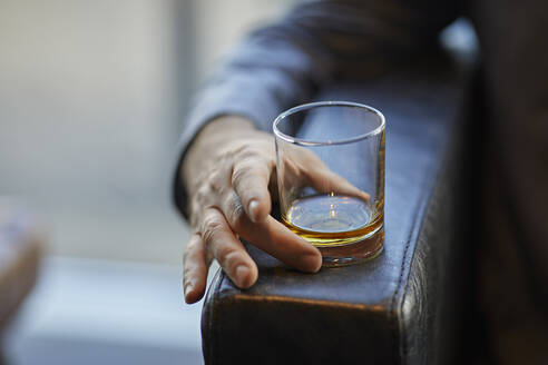 Close-up of man with whiskey glass on arm rest of a leather chair - ZEDF03026