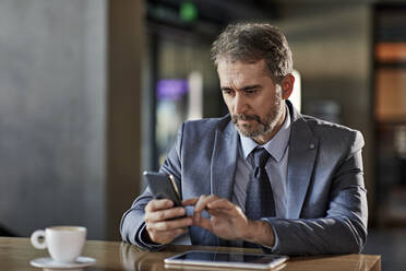 Businessman using smartphone at table - ZEDF03057