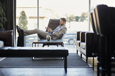 Businessman using smartphone in hotel lobby - ZEDF03068