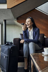 Lächelnde Geschäftsfrau mit Smartphone in der Hotellobby - ZEDF03093
