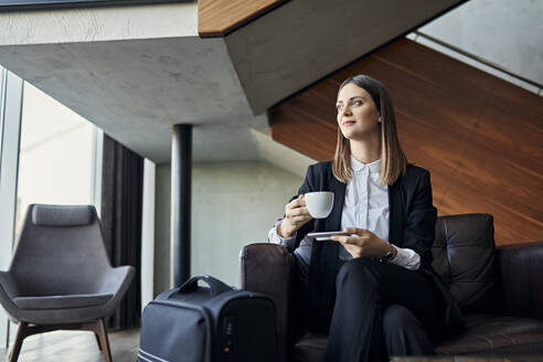 Businesswoman drinking cup of coffee in hotel lobby - ZEDF03094