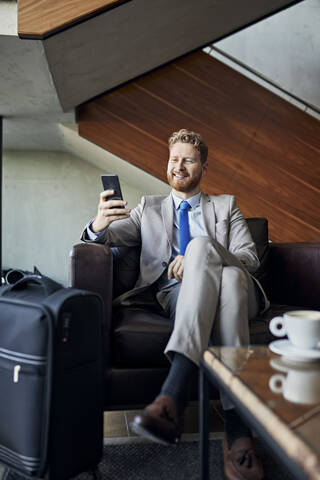 Geschäftsmann benutzt Smartphone in der Hotellobby, lizenzfreies Stockfoto