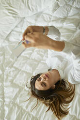 Businesswoman lying on bed using cell phone - ZEDF03108