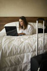 Geschäftsfrau auf dem Bett liegend in einem Hotelzimmer mit Laptop - ZEDF03110