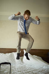 Aufgeregter Geschäftsmann springt auf dem Bett im Hotelzimmer - ZEDF03111