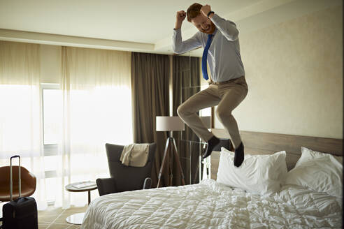 Aufgeregter Geschäftsmann springt auf dem Bett im Hotelzimmer - ZEDF03112