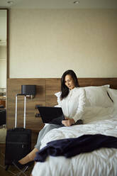 Geschäftsfrau sitzt auf dem Bett im Hotelzimmer und benutzt einen Laptop - ZEDF03121