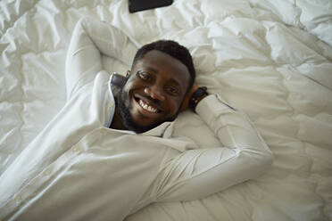 Porträt eines glücklichen Mannes im weißen Hemd, der im Bett liegt - ZEDF03124