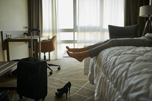 Beine einer Geschäftsfrau auf einem Bett in einem Hotelzimmer liegend - ZEDF03146