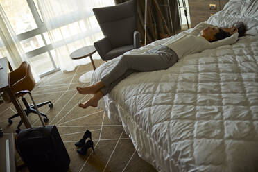 Müde Geschäftsfrau auf dem Bett im Hotelzimmer liegend - ZEDF03147
