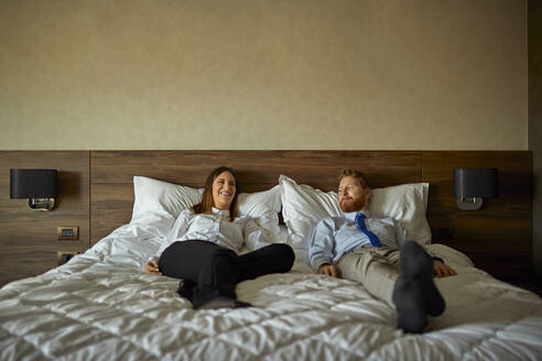 Geschäftsmann und Geschäftsfrau auf dem Bett im Hotelzimmer liegend - ZEDF03149