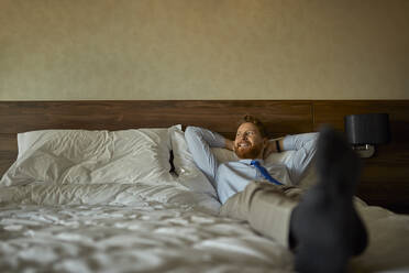 Businessman lying on bed in hotel room - ZEDF03150