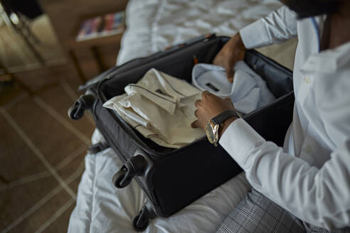 Geschäftsmann sitzt auf dem Bett im Hotelzimmer und packt seinen Koffer - ZEDF03152