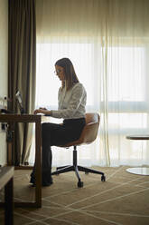 Businesswoman sitting at desk in hotel room using laptop - ZEDF03157