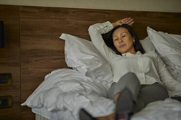 Businesswoman lying on bed in hotel room with closed eyes - ZEDF03165