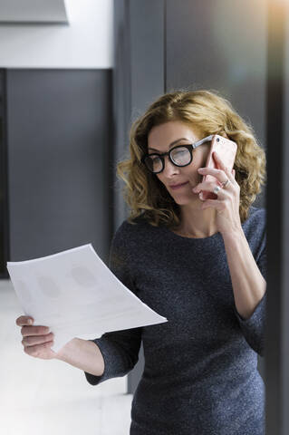 Geschäftsfrau mit Dokumenten in der Hand und Anruf im Büro, lizenzfreies Stockfoto