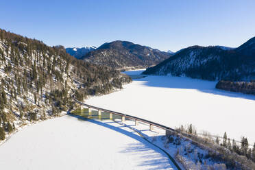 Deutschland, Bayern, Lenggries, Drohnenansicht der Hochstraße über den Sylvenstein-Stausee im Winter - LHF00780