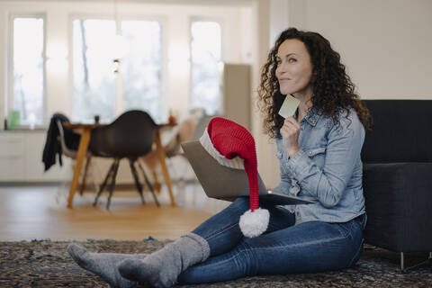 Frau mit Weihnachtsmannmütze, die mit ihrem Laptop online Geschenke kauft, lizenzfreies Stockfoto