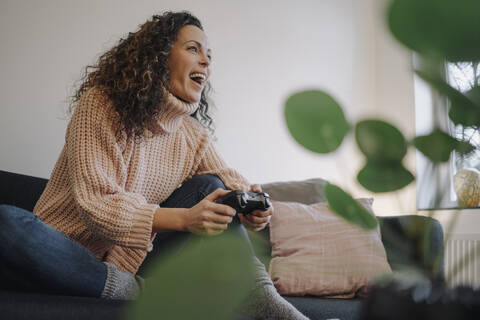 Frau sitzt auf der Couch, hat Spaß und spielt mit einer Spielkonsole, lizenzfreies Stockfoto