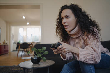 Frau sitzt auf der Couch, hat Spaß und spielt mit einer Spielkonsole - JOSEF00014