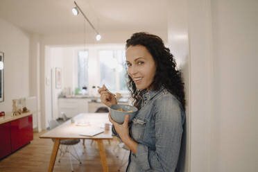 Woman standing in kitchen, eating granola - JOSEF00019