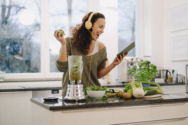 Fit woman standing in kitchen, preparing healthy smoothie, using online recipe - JOSEF00027